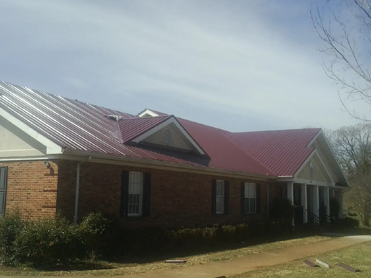 Red metal roof with gabled entries on a long brick building, from a Hail Damage Roof Repair job in Chebeague Island