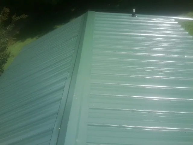 New green metal panels meeting at the ridge of a roof — Flat Roof Repair work by our crew in Chebeague Island