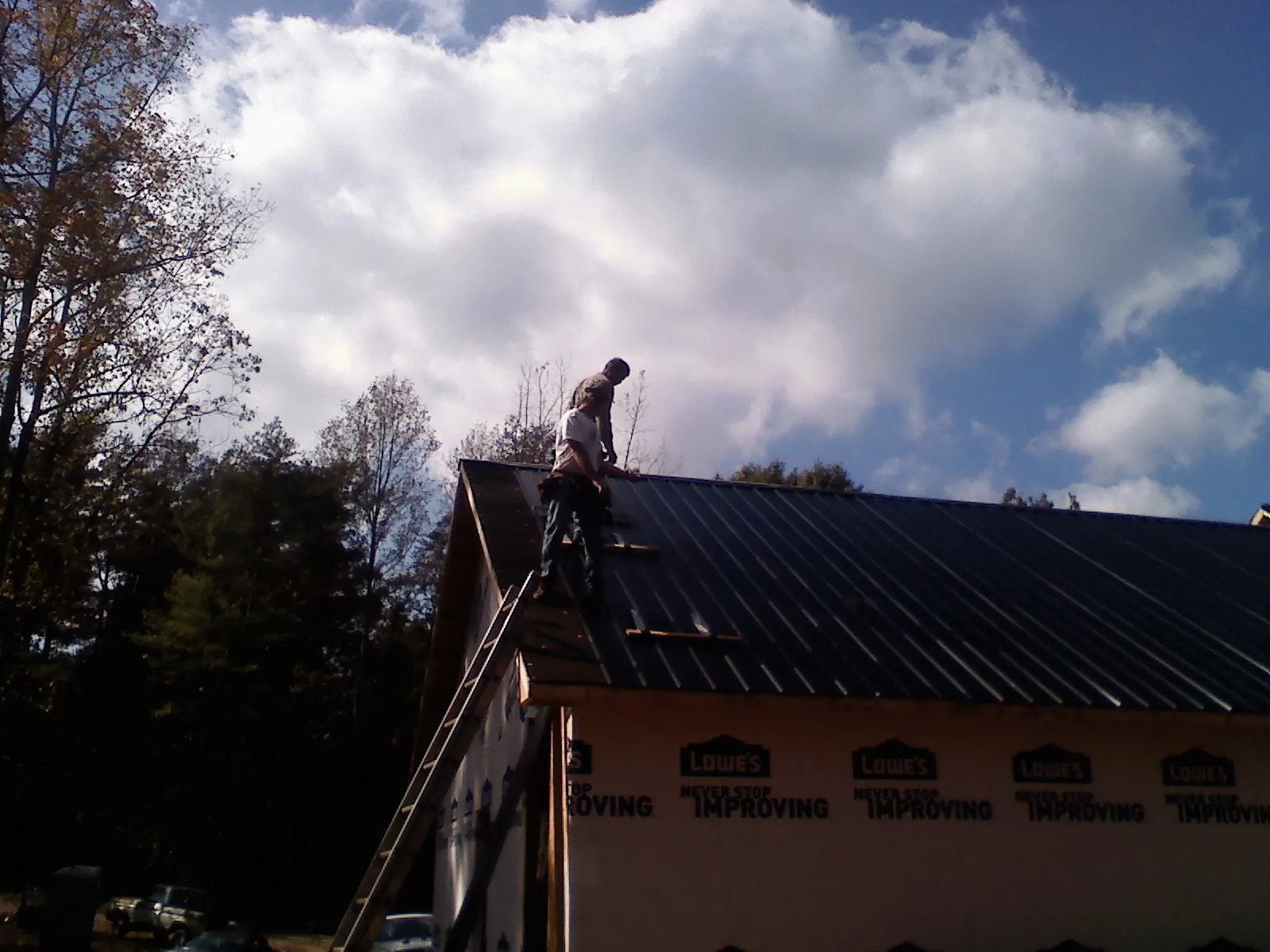 Roofer fastening dark metal panels high against a cloudy sky, from a Roof Inspection job in Chebeague Island
