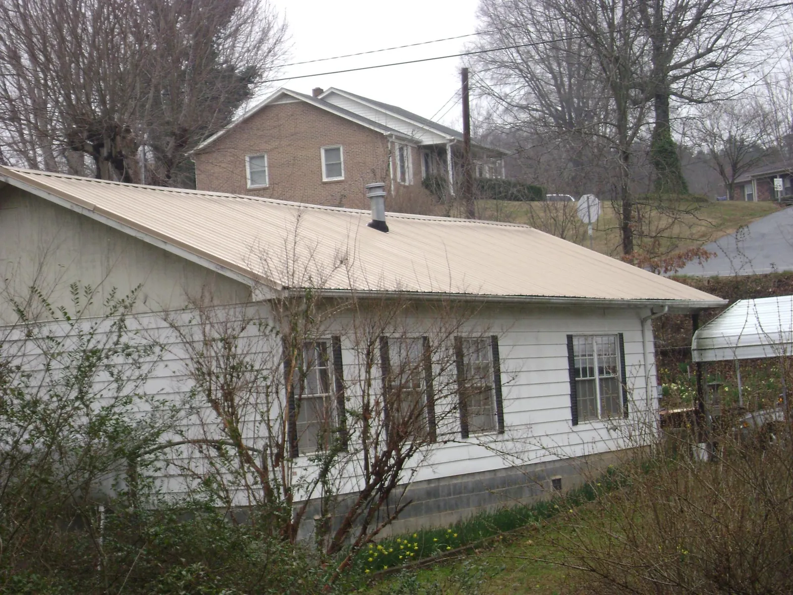 Tan metal roof on a white sided house set into a hillside — Commercial Roofing by Roofing Brothers in Chebeague Island